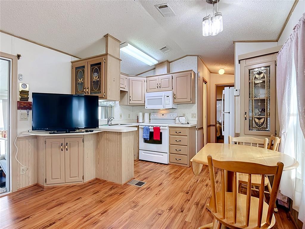 A kitchen and dining area with light wood cabinets, wood-look flooring, and a television stand — 9000 US HWY 192 UNIT 81, CLERMONT, FL