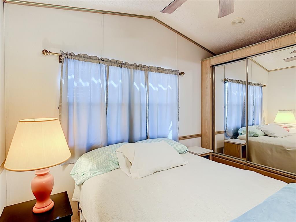 A bedroom features a bed with white bedding, a pink lamp, and mirrored closet doors — 9000 US HWY 192 UNIT 81, CLERMONT, FL