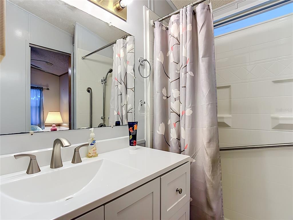 A bathroom features a white vanity, a mirror, and a walk-in shower with grab bars — 9000 US HWY 192 UNIT 81, CLERMONT, FL