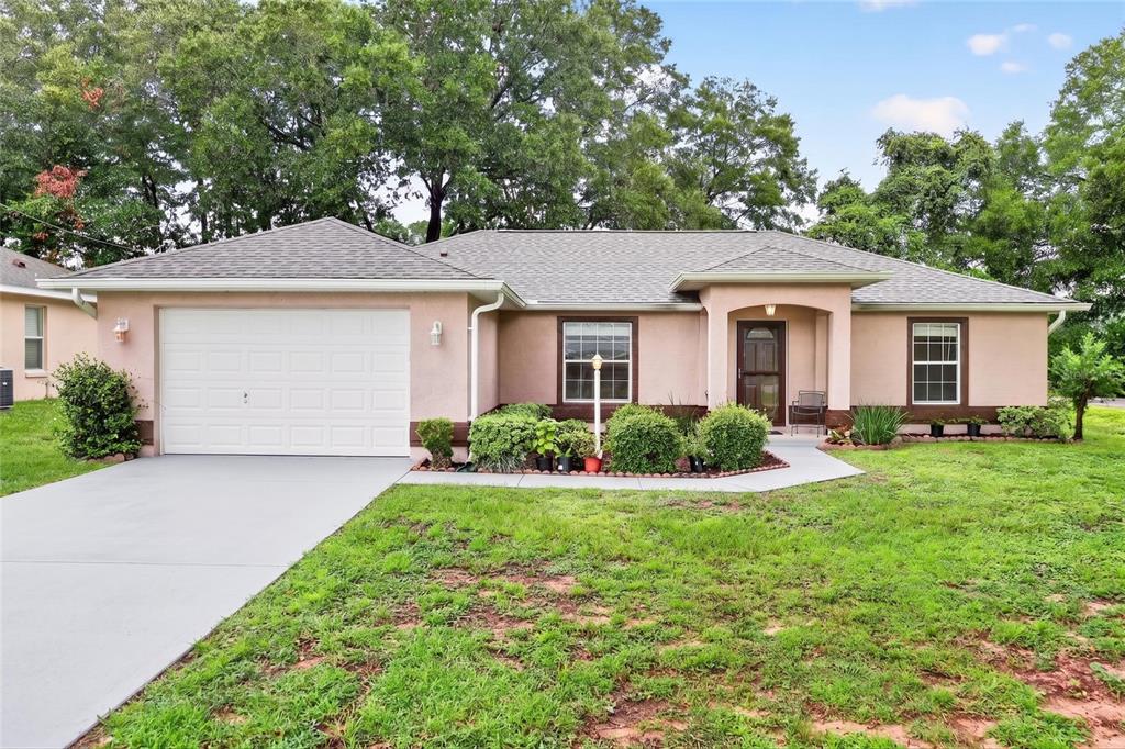 A single-story house with a light pink exterior, a white garage door, and a front porch — 8825 SE 155TH PLACE, SUMMERFIELD, FL