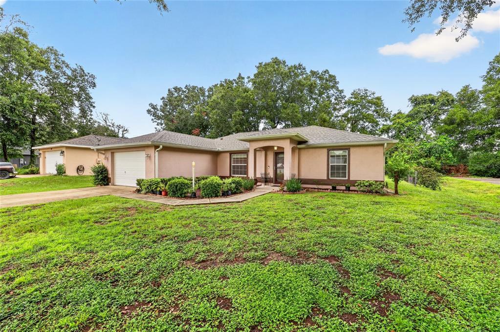 A single-story tan stucco house with a two-car garage and a large grassy front yard — 8825 SE 155TH PLACE, SUMMERFIELD, FL