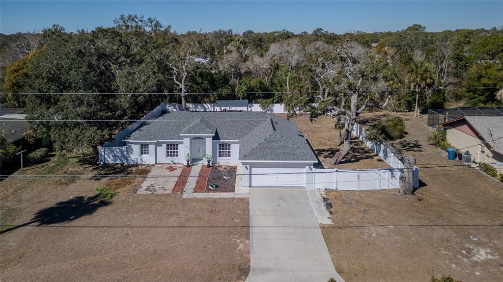 An aerial view shows a single-story house with a gray roof, white siding, and driveway — 1007 TRYON CIRCLE, SPRING HILL, FL