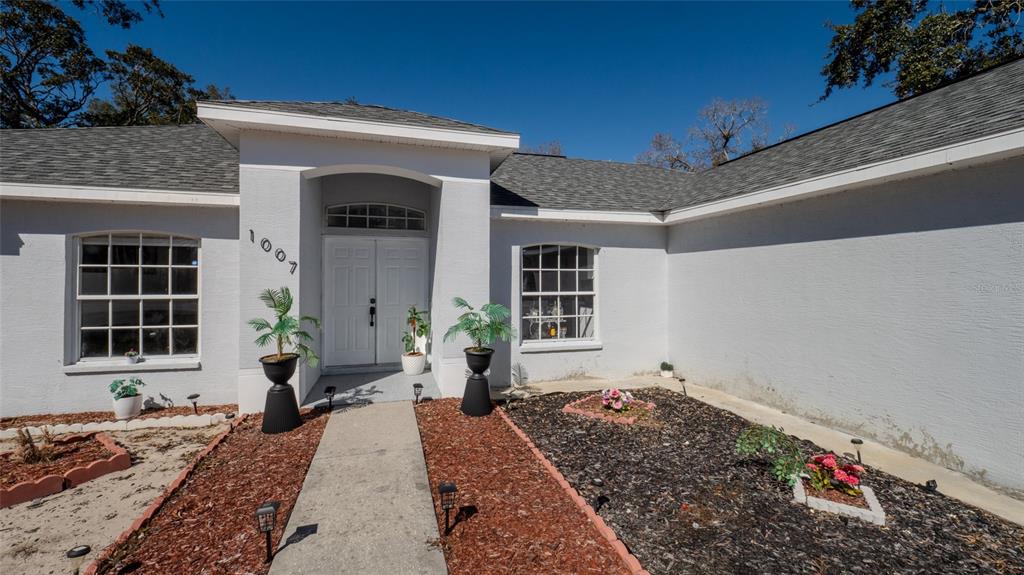 The exterior of a white single-story house features a front walkway, landscaping, and double doors — 1007 TRYON CIRCLE, SPRING HILL, FL