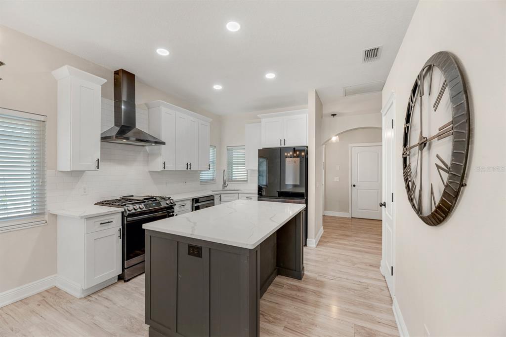 A modern kitchen features white cabinets, a dark gray island, and stainless steel appliances — 6116 SKYLARKCREST DRIVE, LITHIA, FL