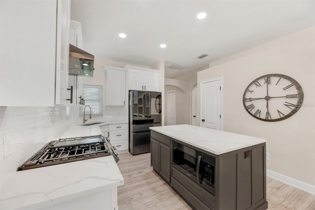 A kitchen features white cabinets, a dark gray island with a microwave, and quartz countertops — 6116 SKYLARKCREST DRIVE, LITHIA, FL
