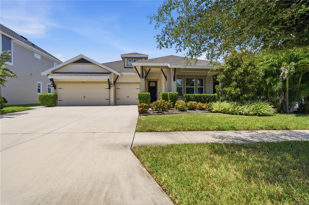 A single-story house with a three-car garage, tan stucco exterior, and a manicured front lawn — 7720 PARADISO DRIVE, APOLLO BEACH, FL