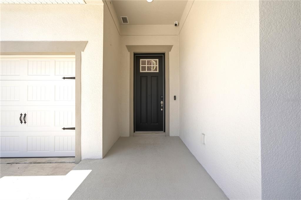 A covered entryway features a black front door with a window and a white garage — 7720 PARADISO DRIVE, APOLLO BEACH, FL
