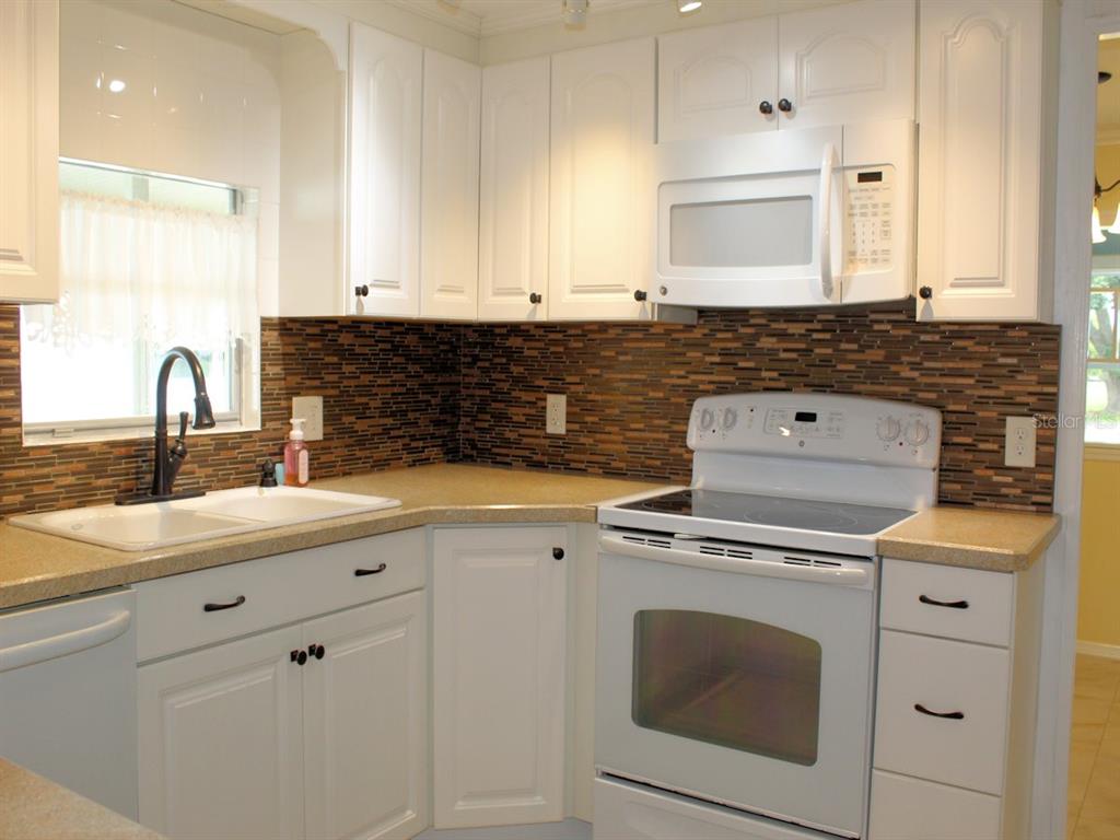 A kitchen features white cabinets, a tan countertop, a white stove, and a brown tiled backsplash — 92 THATCH PALM STREET E, LARGO, FL