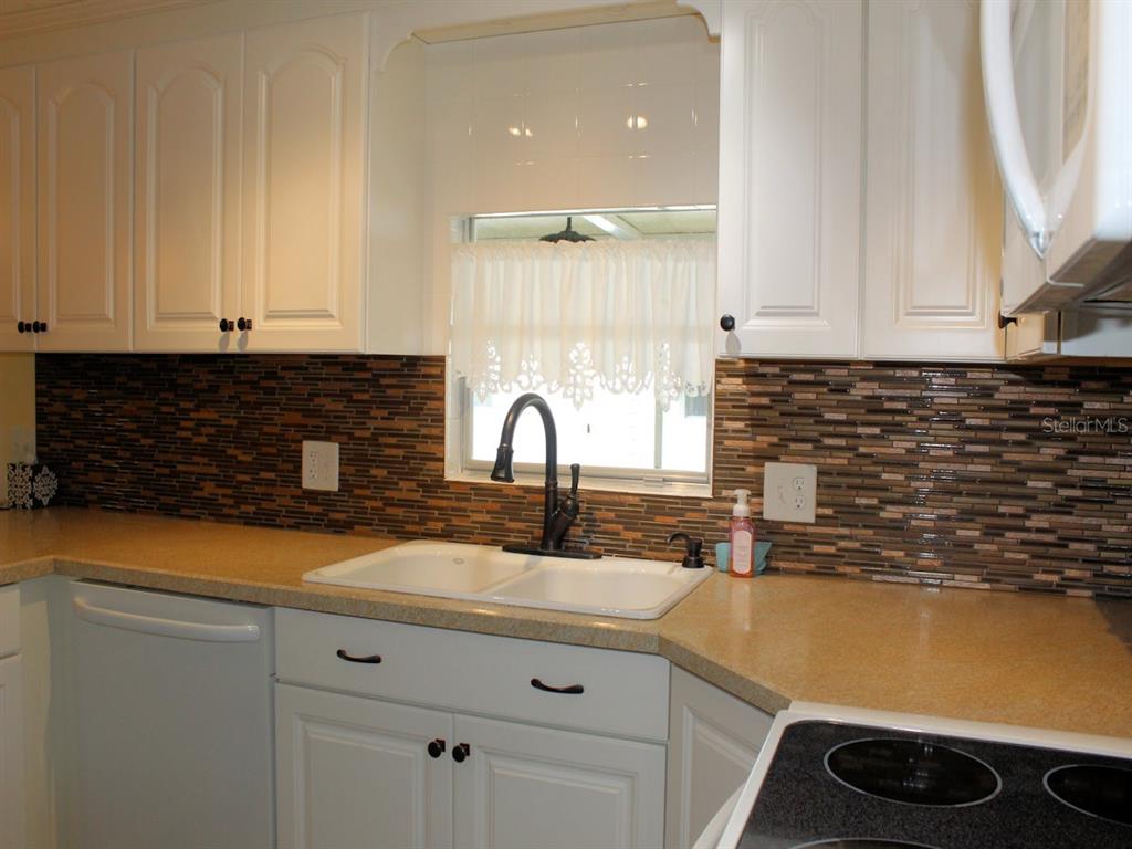 A kitchen features white cabinets, a tan countertop, a dark tiled backsplash, and a double sink — 92 THATCH PALM STREET E, LARGO, FL