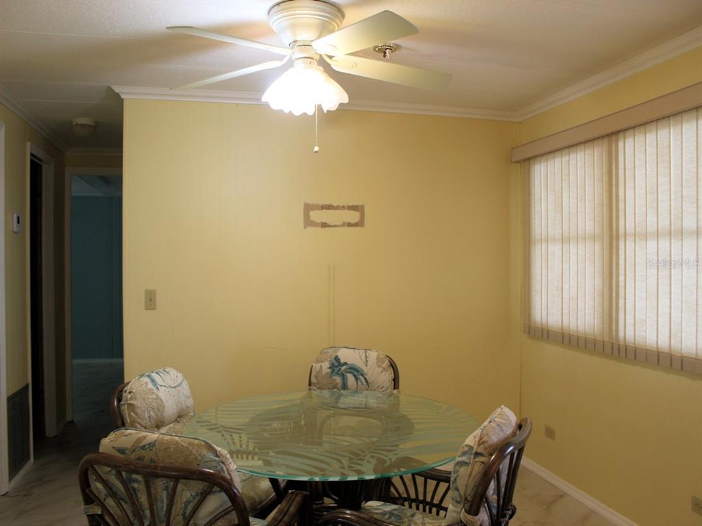 A dining area with a glass-topped table, rattan chairs, yellow walls, and a ceiling fan — 92 THATCH PALM STREET E, LARGO, FL