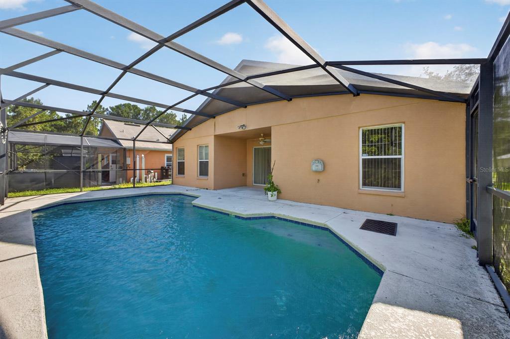A screened-in swimming pool and patio area behind a tan stucco house — 839 SANDY RIDGE DRIVE, DAVENPORT, FL