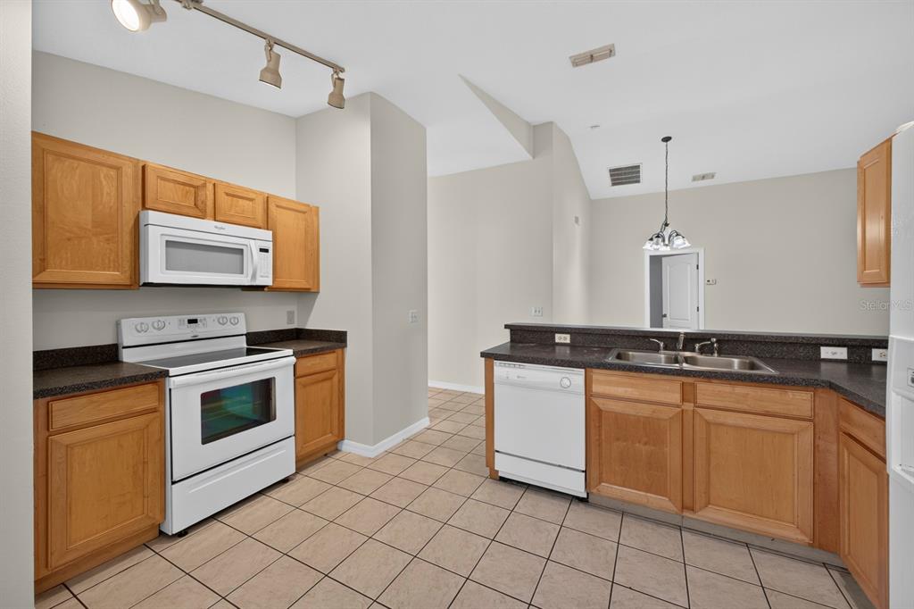 A kitchen with light wood cabinets, dark countertops, white appliances, and beige tile flooring — 839 SANDY RIDGE DRIVE, DAVENPORT, FL