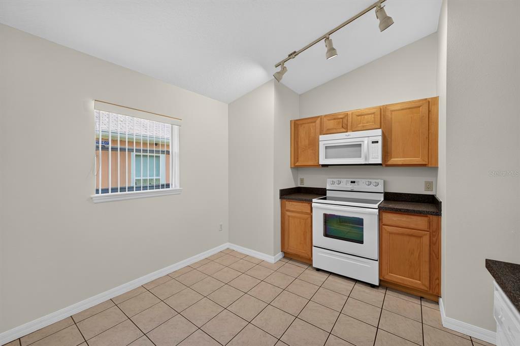 A kitchen features light wood cabinets, white appliances, dark countertops, and beige tile flooring — 839 SANDY RIDGE DRIVE, DAVENPORT, FL