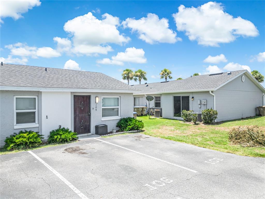 The exterior of a single-story residential building features gray siding, a shingled roof, and parking — 106 LAKE VILLA WAY, KISSIMMEE, FL