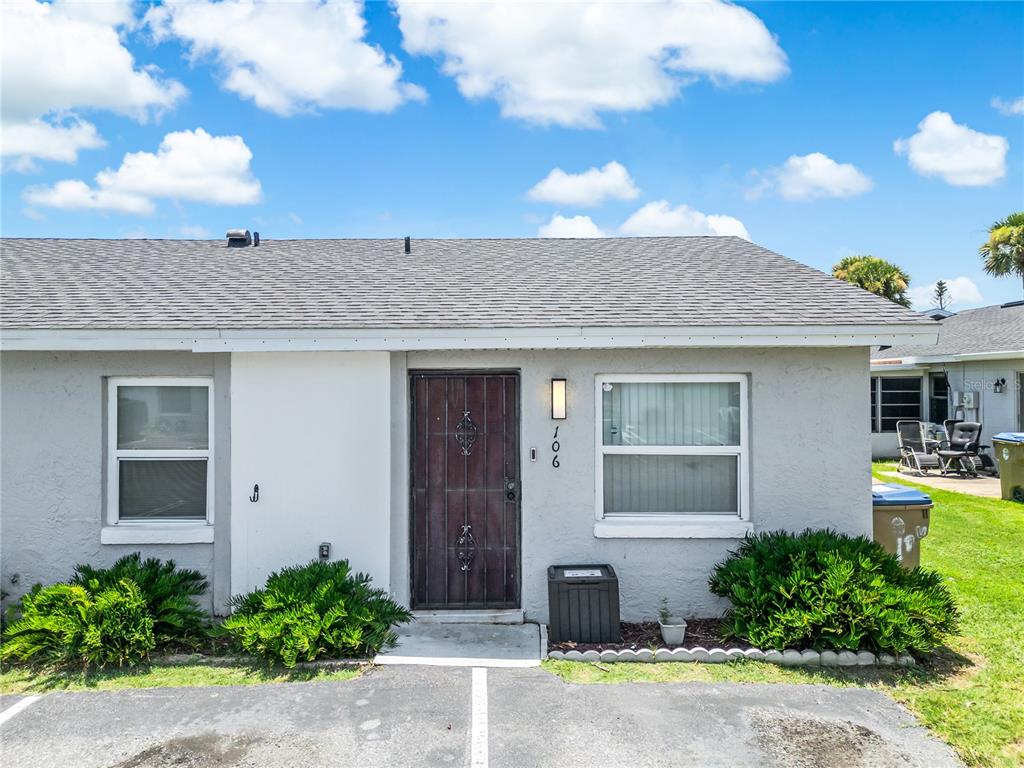 A gray single-story residential building exterior features a dark metal front door and two windows — 106 LAKE VILLA WAY, KISSIMMEE, FL
