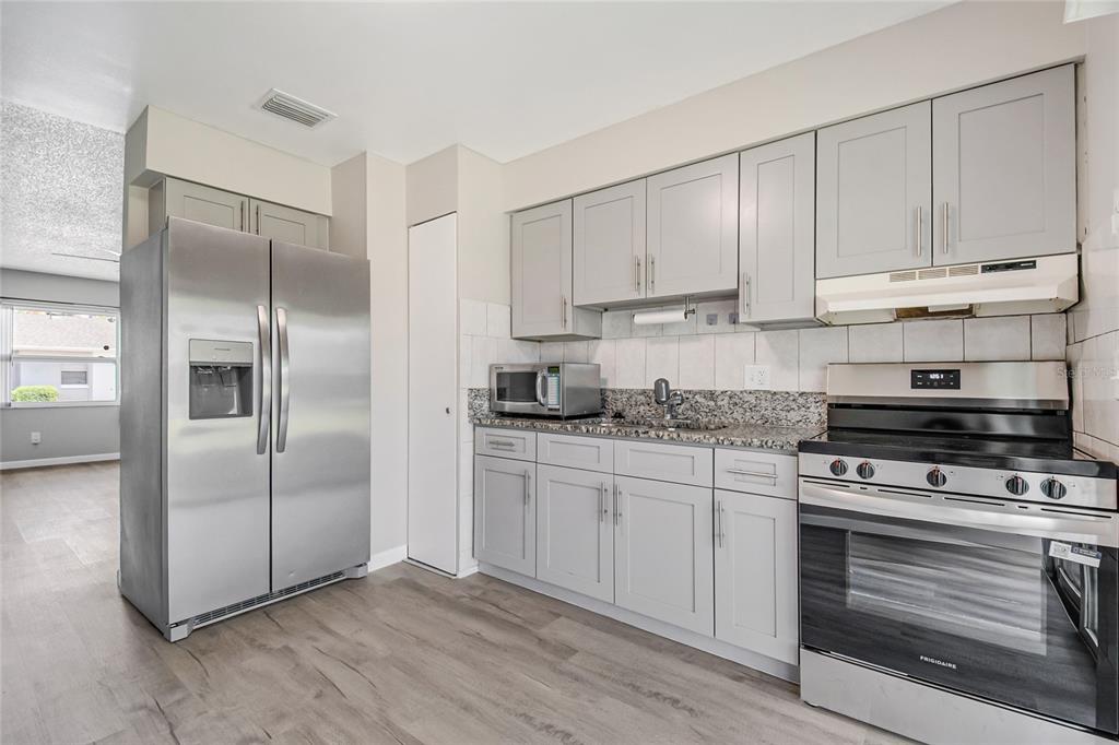 A kitchen features gray cabinets, granite countertops, stainless steel appliances, and light wood-look flooring — 106 LAKE VILLA WAY, KISSIMMEE, FL