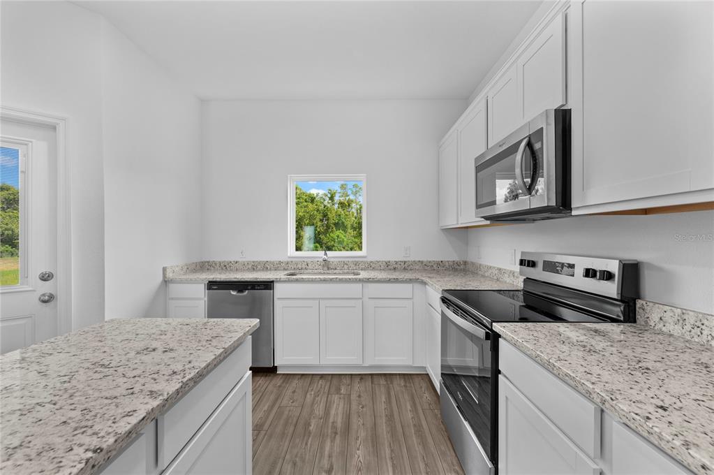 A kitchen features white cabinets, granite countertops, stainless steel appliances, and wood-look flooring — 576 BAY LEAF DRIVE, POINCIANA, FL