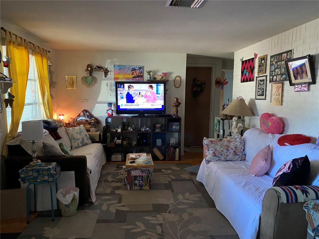 A living room features two sofas, a television on a shelving unit, and yellow curtains — 10018 CHERRY CREEK LANE, PORT RICHEY, FL