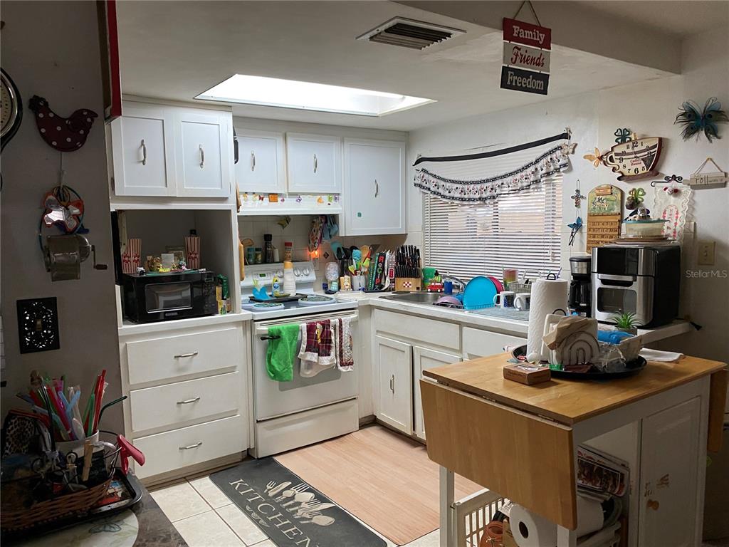 A kitchen with white cabinets, a white stove, a skylight, and a wooden island — 10018 CHERRY CREEK LANE, PORT RICHEY, FL