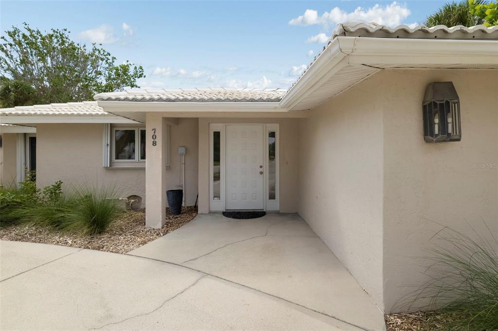 The exterior of a beige house features a covered entryway with a white front door — 708 GARFIELD DRIVE, SARASOTA, FL