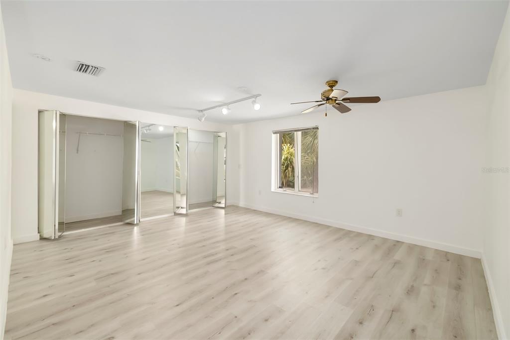 A bedroom with light wood-look flooring, mirrored closet doors, a ceiling fan, and a window — 708 GARFIELD DRIVE, SARASOTA, FL