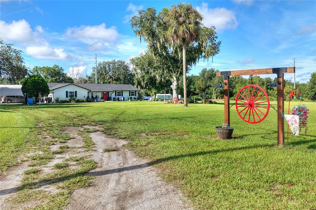 A large grassy yard features a dirt driveway, a red wagon wheel decoration, and a house — 4220 HOWELL LANE, MULBERRY, FL