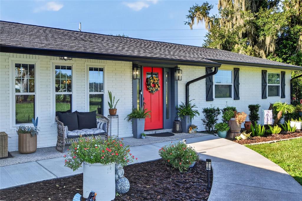 A white brick house exterior features a bright red front door and a front porch — 4220 HOWELL LANE, MULBERRY, FL