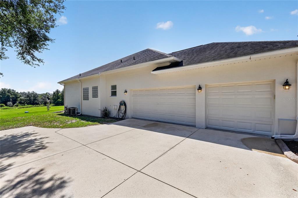 A side view of a house exterior featuring a three-car garage and a concrete driveway — 32542 SCENIC HILLS DRIVE, MOUNT DORA, FL