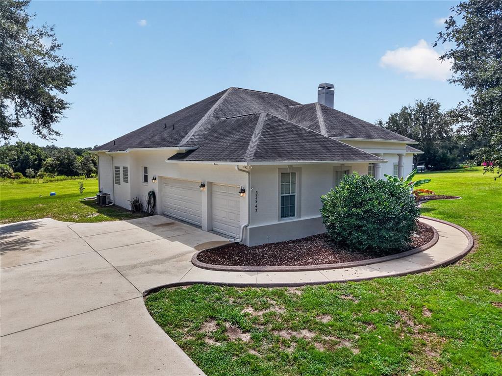 An exterior view of a single-story house featuring a two-car garage and a concrete driveway — 32542 SCENIC HILLS DRIVE, MOUNT DORA, FL