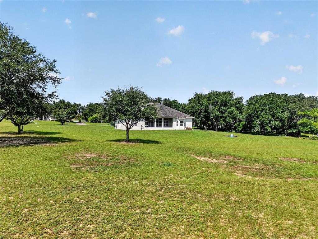 A white house with a screened-in porch sits on a large, grassy, tree-lined lot — 32542 SCENIC HILLS DRIVE, MOUNT DORA, FL
