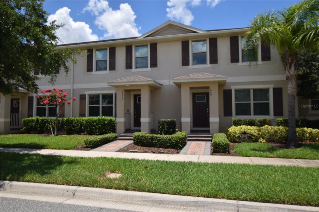 A two-story townhouse exterior features beige stucco walls, dark shutters, and two covered entryways — 16097 PEBBLE BLUFF LOOP, WINTER GARDEN, FL