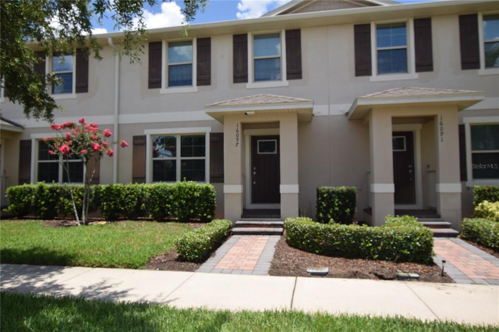A two-story townhouse exterior features beige stucco walls, dark brown shutters, and brick walkways — 16097 PEBBLE BLUFF LOOP, WINTER GARDEN, FL