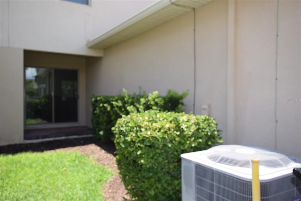 An exterior view shows a beige wall, a sliding glass door, bushes, and an air conditioner — 16097 PEBBLE BLUFF LOOP, WINTER GARDEN, FL