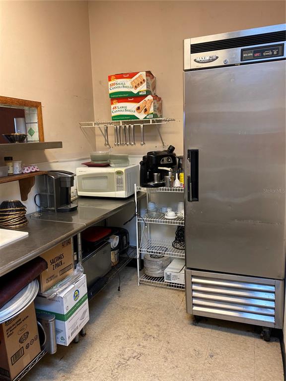 A commercial kitchen area features a stainless steel refrigerator, microwave, coffee maker, and shelving units — 883 WEST BAY DRIVE, LARGO, FL
