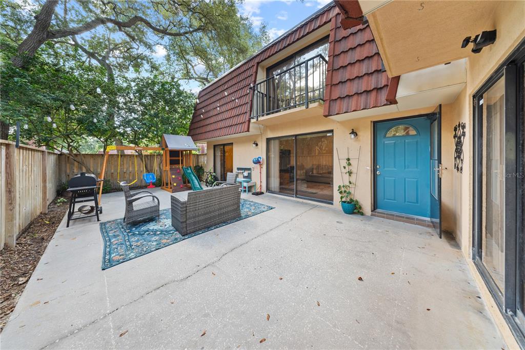 A concrete patio features a small playground, outdoor seating, and a blue door on the house — 680 1ST COURT, PALM HARBOR, FL