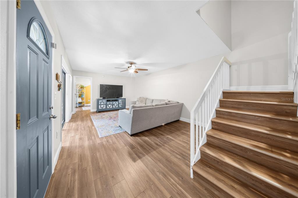 A living room with wood-look flooring, a gray sofa, and a staircase with white railings — 680 1ST COURT, PALM HARBOR, FL