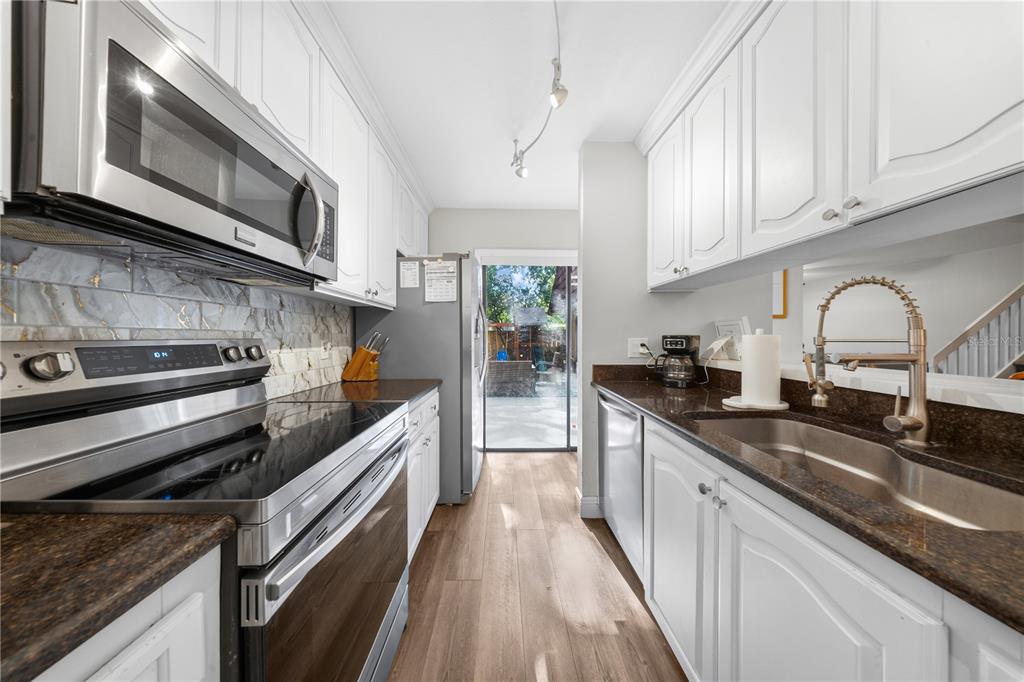 A galley kitchen features white cabinets, stainless steel appliances, dark countertops, and a sliding glass door — 680 1ST COURT, PALM HARBOR, FL
