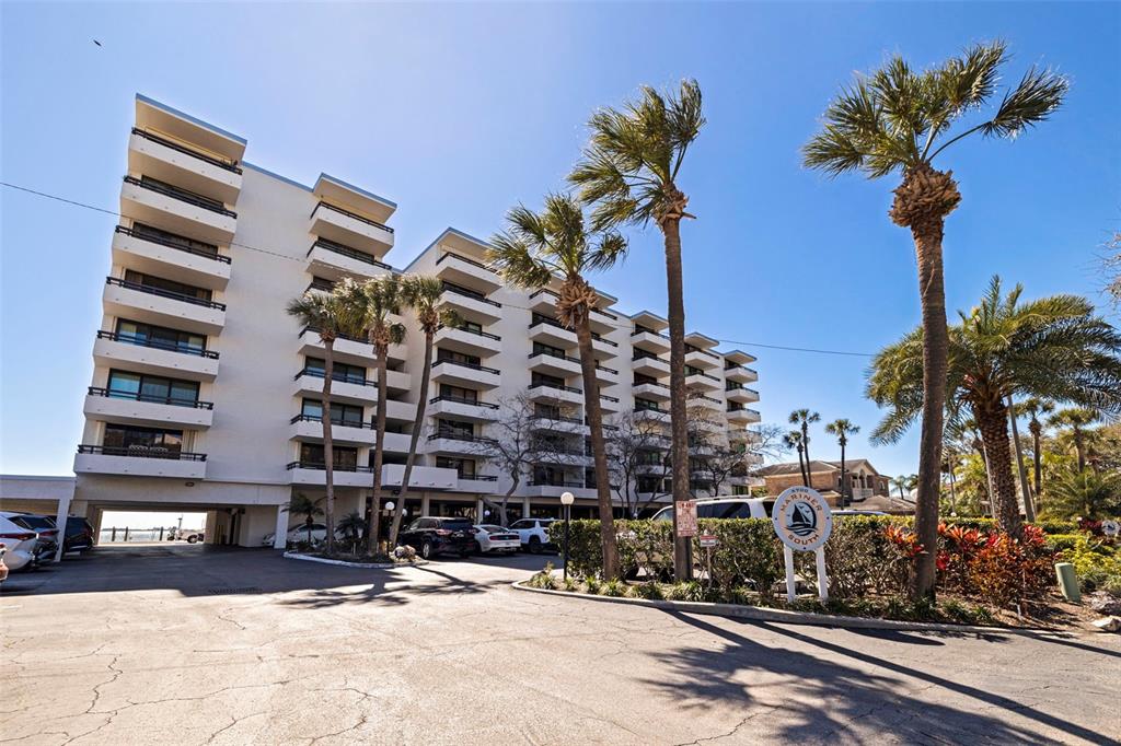 A multi-story white apartment building stands behind a parking lot with palm trees — 5700 MARINER STREET UNIT 803, TAMPA, FL