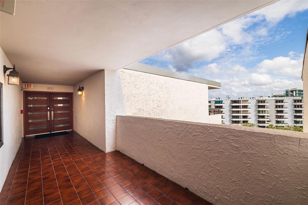 A tiled outdoor balcony leads to a double-door entrance with a view of nearby buildings — 5700 MARINER STREET UNIT 803, TAMPA, FL