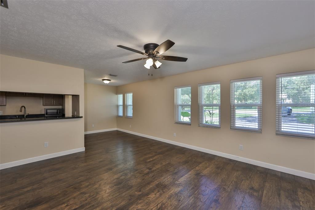 A living room with dark wood flooring, beige walls, a ceiling fan, and large windows — 105 N KINGSWAY ROAD, SEFFNER, FL