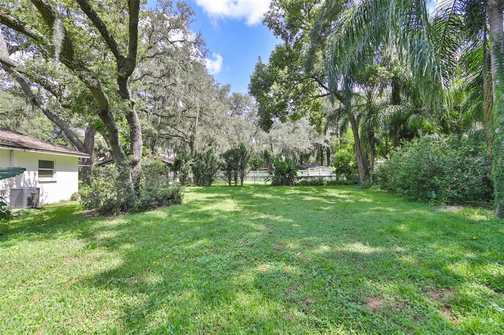 A grassy backyard features mature trees, a white house exterior, and dense perimeter landscaping — 105 N KINGSWAY ROAD, SEFFNER, FL