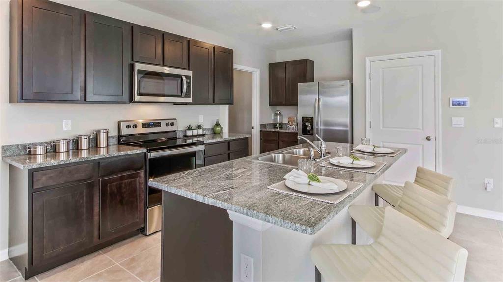 A kitchen features dark wood cabinets, granite countertops, stainless steel appliances, and a breakfast island — 4540 HIDDEN FARM DRIVE, PLANT CITY, FL