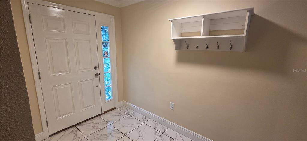 An entryway features a white door with a stained-glass sidelight, marble-look tile flooring, and shelving — 225 YARMOUTH ROAD, FERN PARK, FL