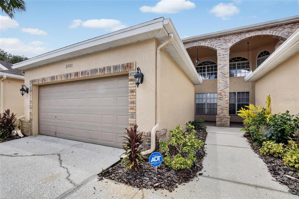 The exterior of a two-story house features a tan stucco facade, brick accents, and a garage — 2205 PRESERVATION DRIVE, PLANT CITY, FL
