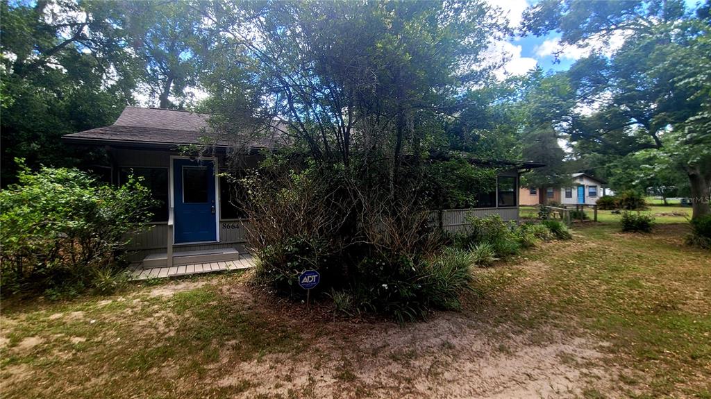 A gray house with a blue door sits in a wooded yard with an ADT sign — 8664 CR 639, BUSHNELL, FL