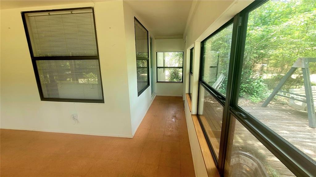 A sunroom with orange flooring, white walls, and large windows overlooking a wooden deck — 8664 CR 639, BUSHNELL, FL