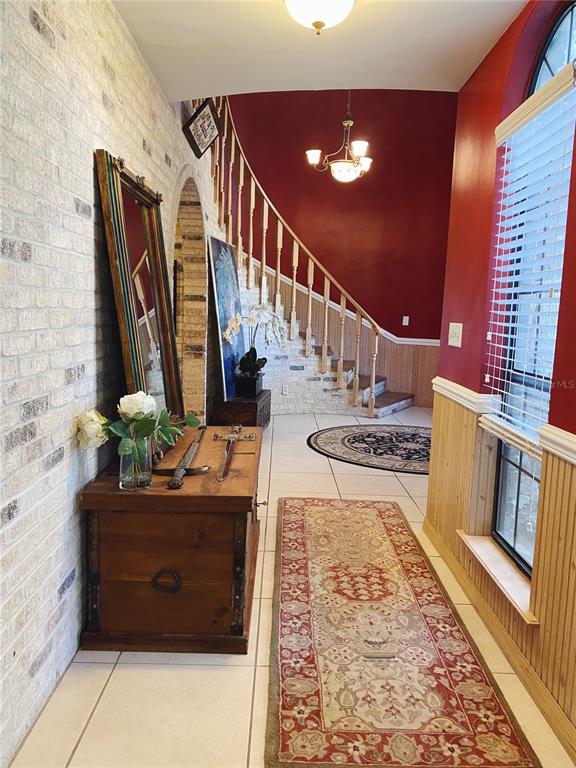 A foyer features a curved staircase, a brick wall, a wooden chest, and tile flooring — 27 LAKE VISTA WAY, ORMOND BEACH, FL