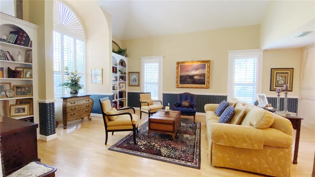 A living room features light wood floors, built-in shelving, a large rug, and yellow furniture — 27 LAKE VISTA WAY, ORMOND BEACH, FL