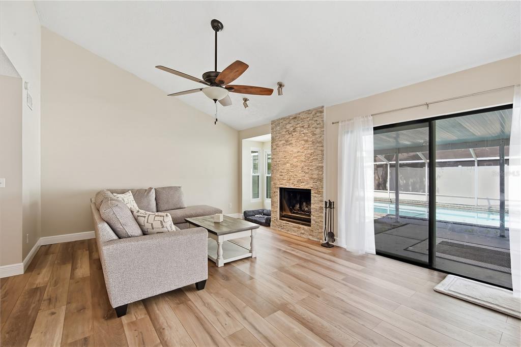 A living room with wood-look flooring, a stone fireplace, and sliding glass doors to a pool — 4509 GRAINARY AVENUE, TAMPA, FL