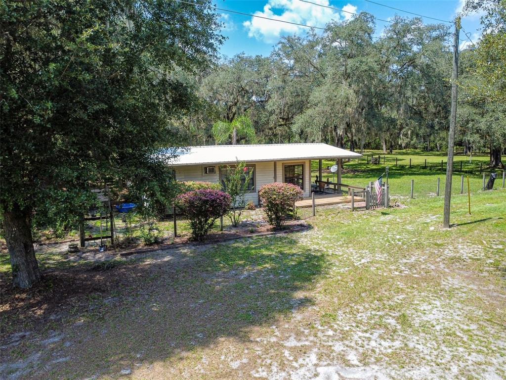 A single-story house with a metal roof and wooden deck sits in a wooded yard — 28622 N STATE ROAD 121, ALACHUA, FL